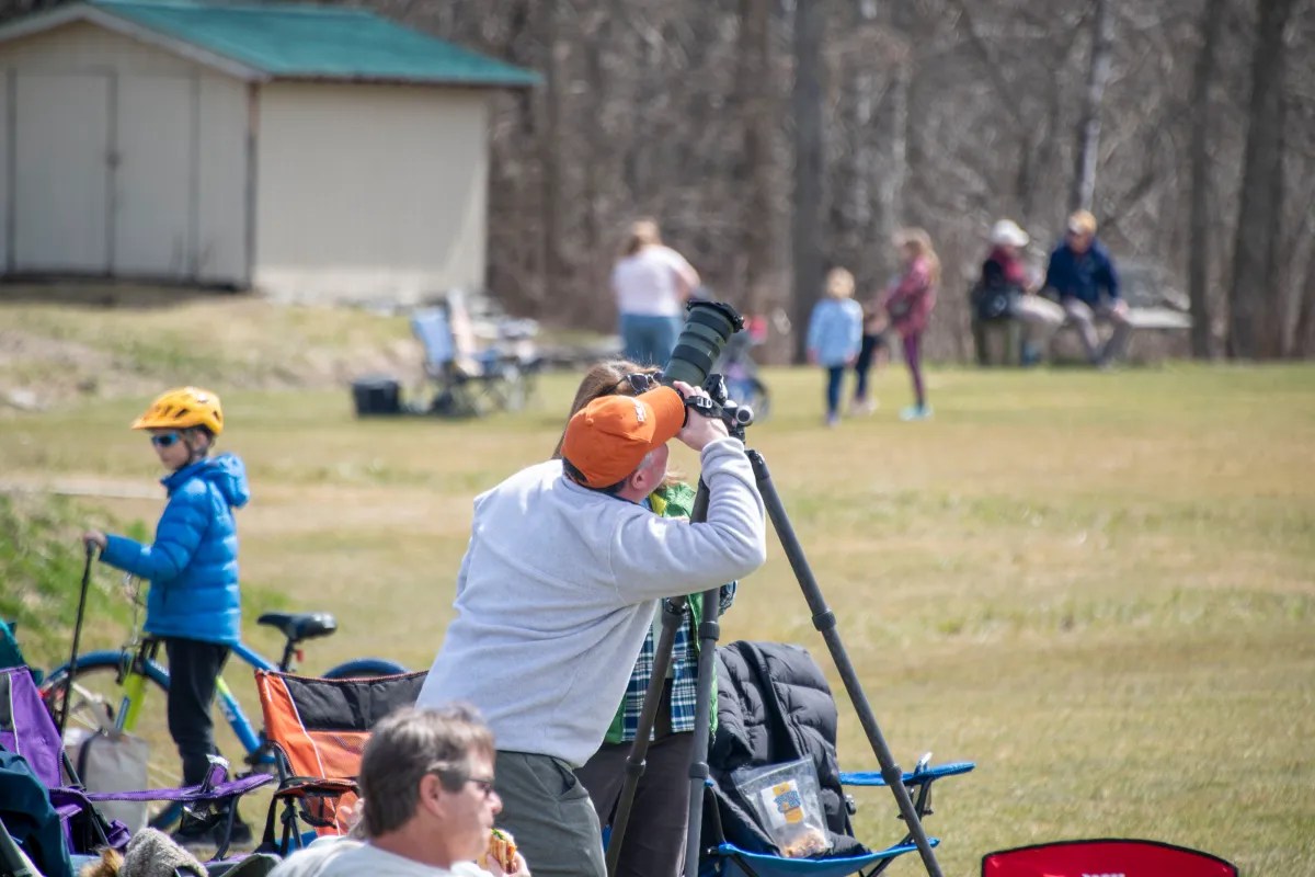 A photographer taking pictures at an outdoor event with spectators in the background.