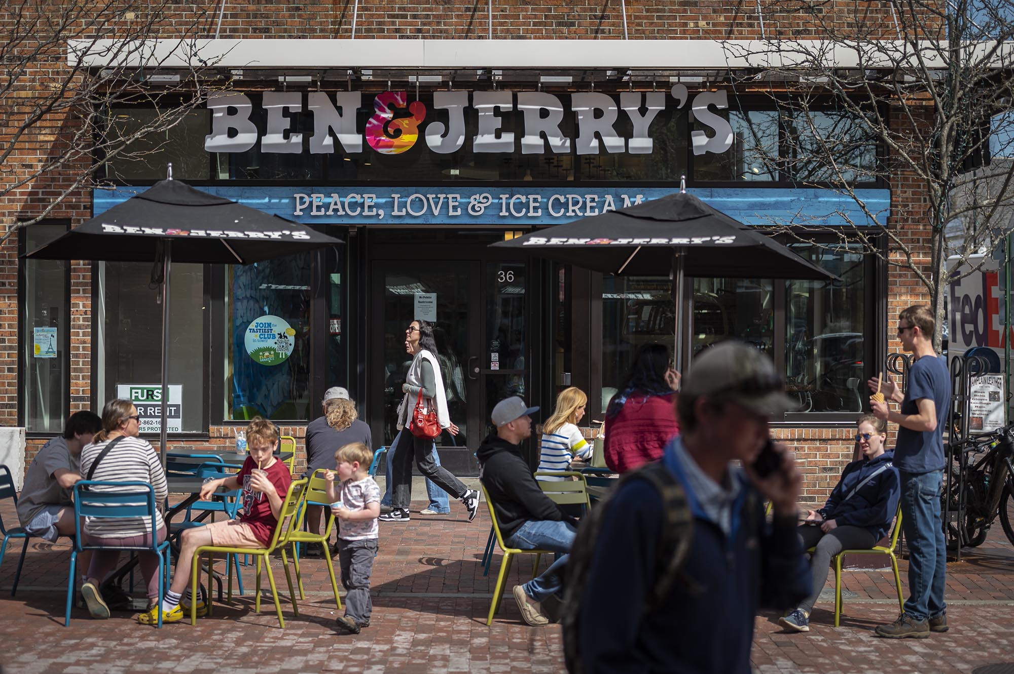 People sitting outside a Ben & Jerry's ice cream shop on a sunny day, with pedestrians walking past.