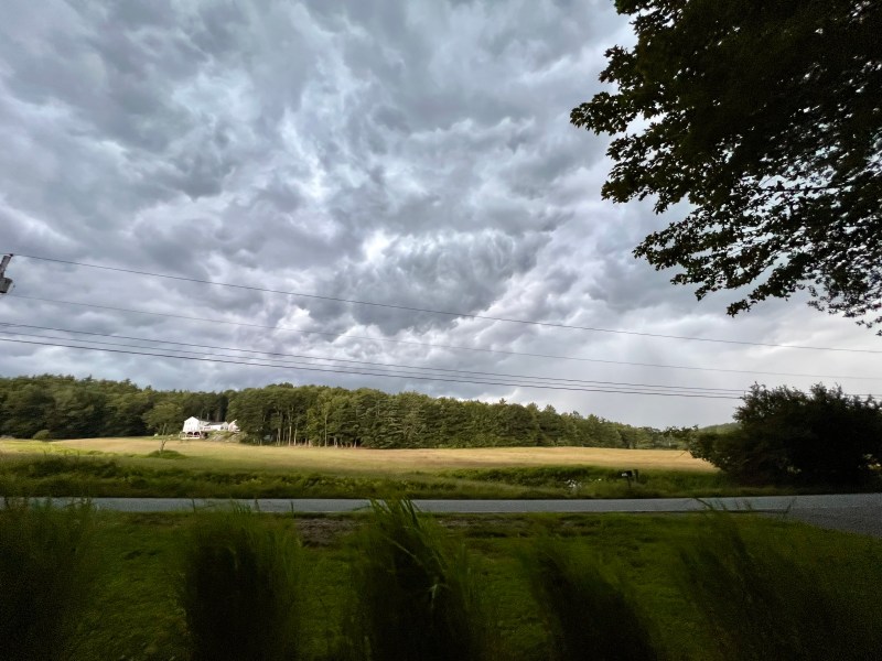a cloudy sky over a field and trees.