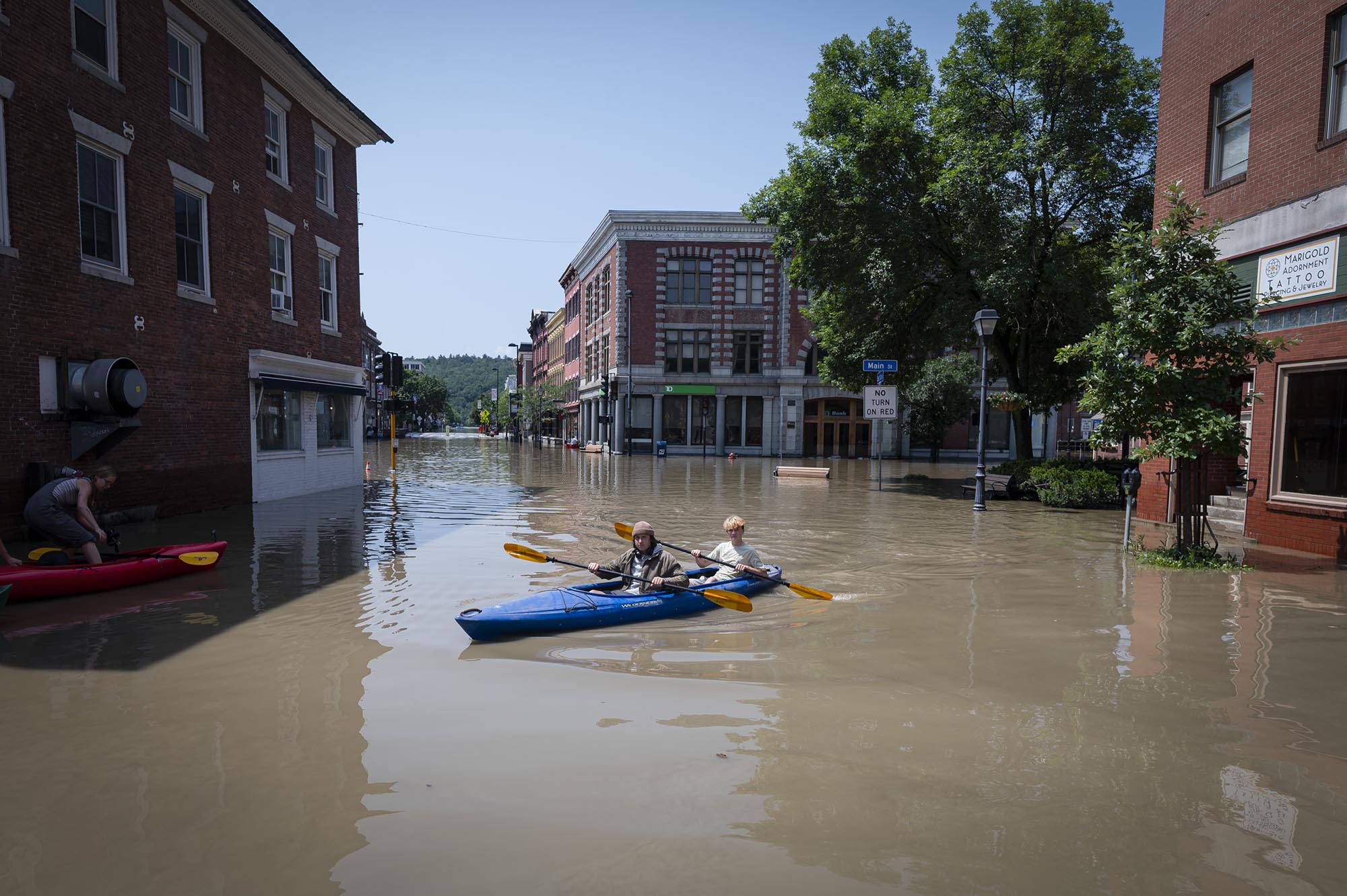 two people in kayaks paddling down a flooded street.