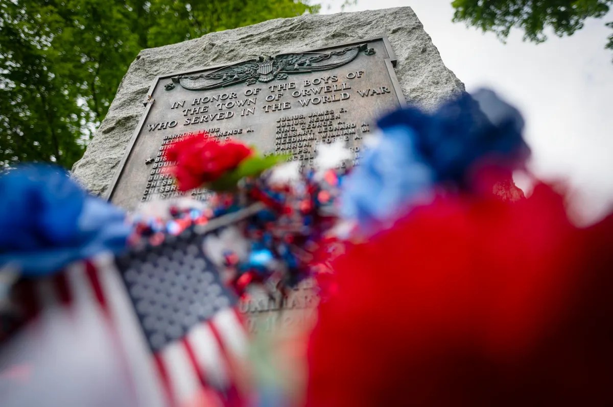 A stone memorial honors local soldiers who served in World War I, with flowers and American flags placed in front.
