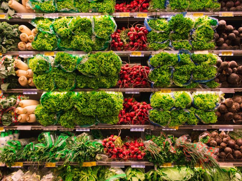 A produce shelf with greens and radishes at a grocery store.