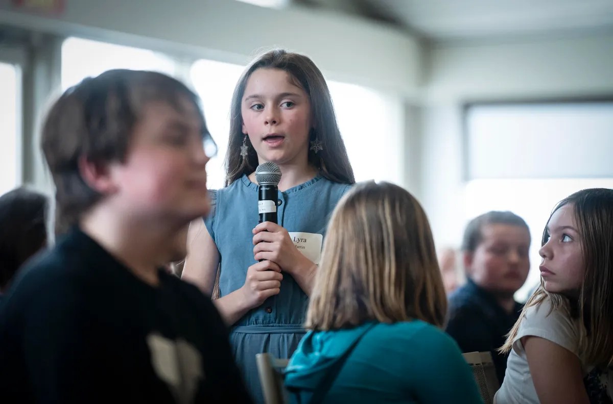A young girl speaks into a microphone during a group discussion as other participants listen.