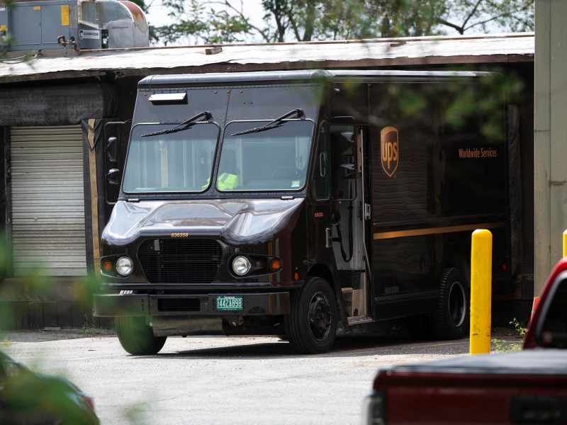 A UPS delivery truck is parked outside a loading dock near a building with a closed garage door.