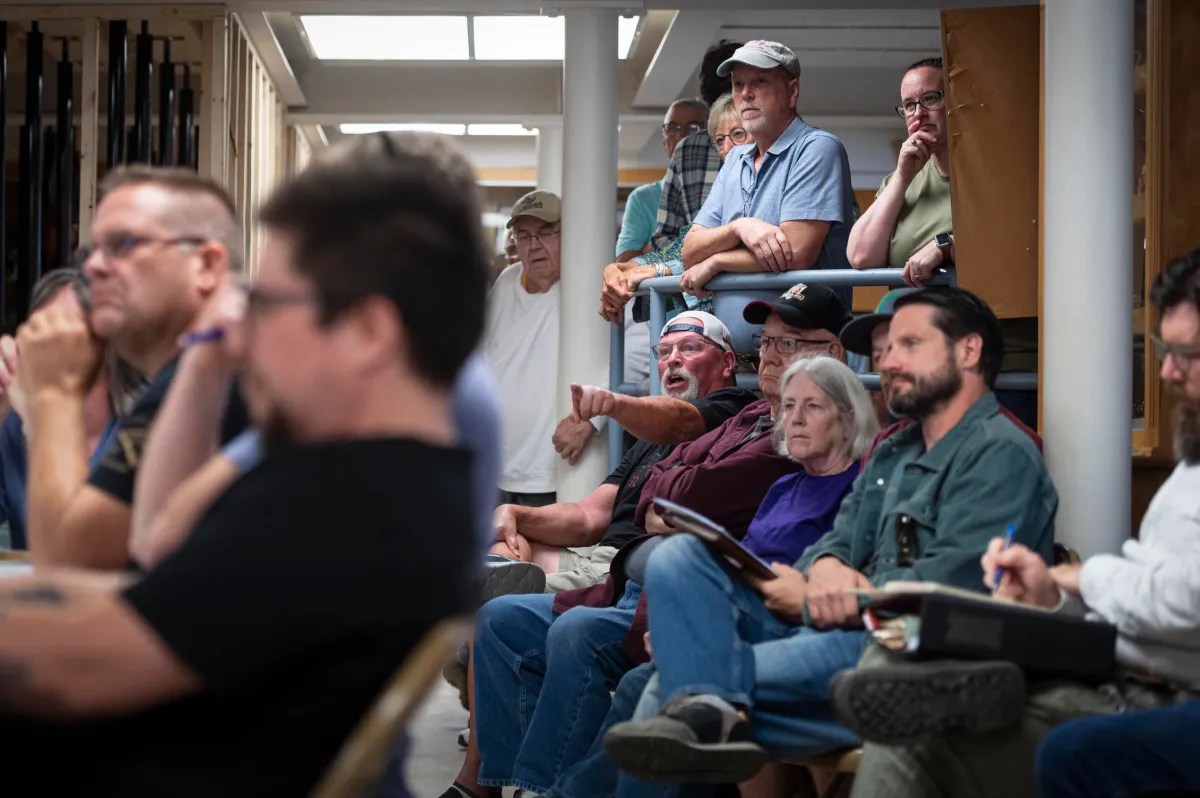 A group of people attentively watch and take notes during a meeting or public discussion held indoors.