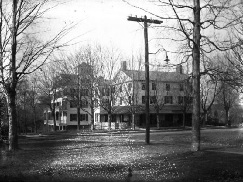 Black and white photo of a large, multi-story house with a covered porch, bare trees, and a utility pole in the foreground.
