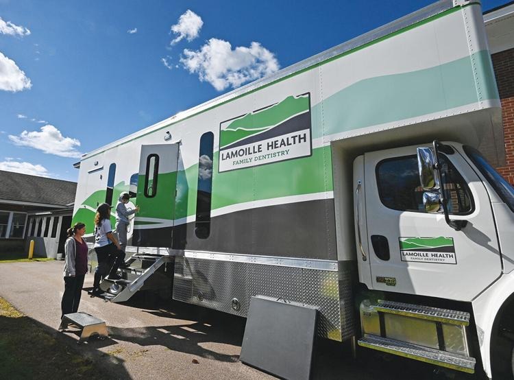 A mobile dental clinic truck labeled "Lamoille Health Family Dentistry" parked outside, with two people entering via steps.